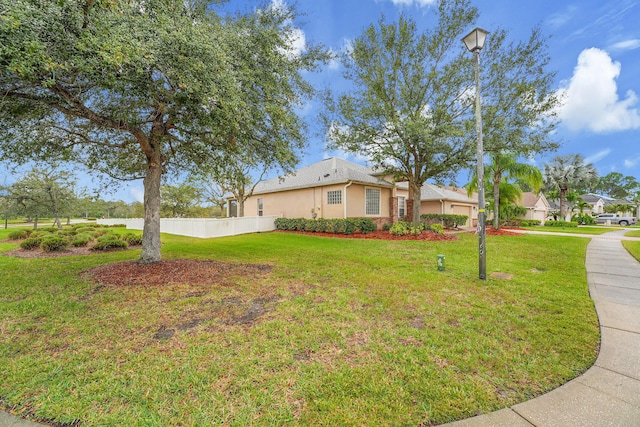 view of front facade with an attached garage, stucco siding, fence, and a front yard