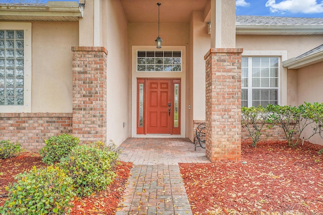 view of exterior entry featuring stucco siding, a shingled roof, and brick siding