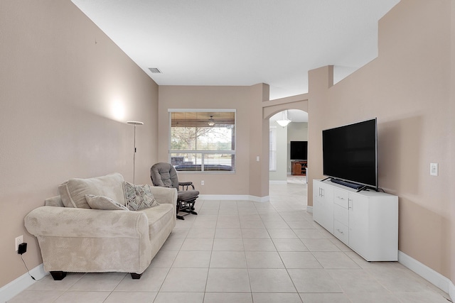 living room featuring arched walkways, light tile patterned floors, visible vents, and baseboards