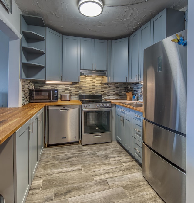 kitchen featuring wood counters, appliances with stainless steel finishes, blue cabinets, and backsplash