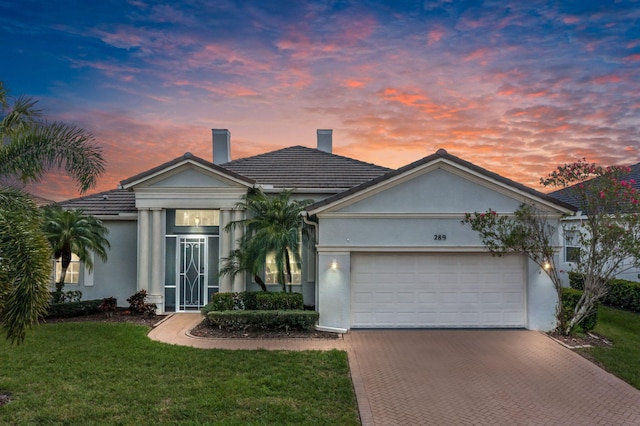 ranch-style house with stucco siding, a chimney, an attached garage, decorative driveway, and a front yard