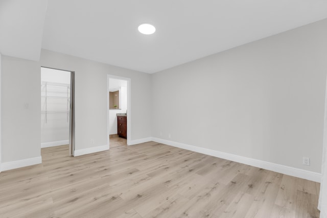 unfurnished bedroom with ensuite bathroom, a spacious closet, a closet, and light wood-type flooring