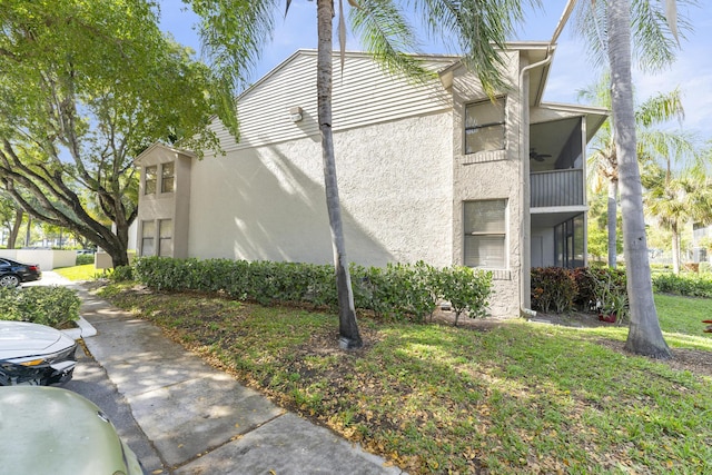 view of side of property featuring ceiling fan, a yard, and a balcony