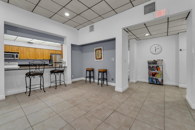 kitchen featuring appliances with stainless steel finishes, a breakfast bar, light tile patterned floors, and a drop ceiling