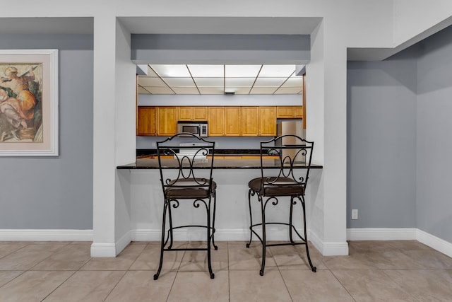 kitchen with stainless steel appliances, a breakfast bar, light tile patterned floors, and kitchen peninsula