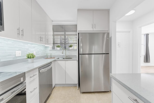 kitchen featuring sink, stainless steel appliances, light stone countertops, decorative backsplash, and white cabinets