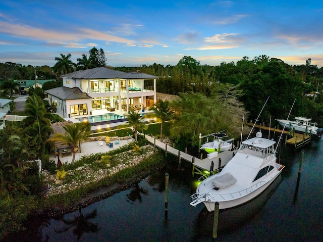 rear view of property with a water view, a balcony, boat lift, an outdoor pool, and a patio