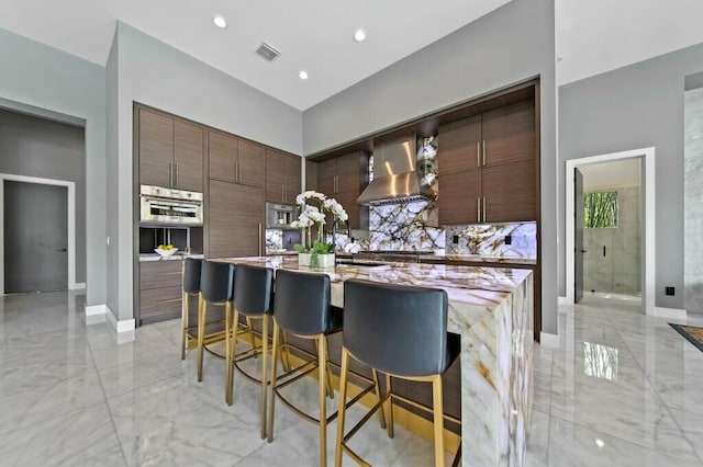 kitchen featuring marble finish floor, visible vents, stainless steel oven, wall chimney range hood, and modern cabinets