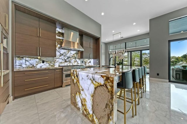 kitchen featuring a kitchen island with sink, marble finish floor, high end stainless steel range oven, backsplash, and wall chimney exhaust hood