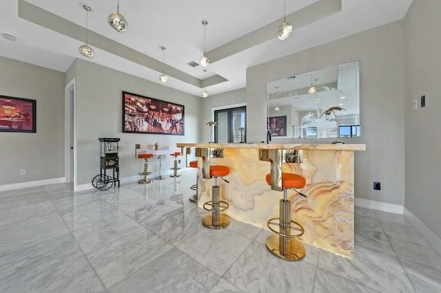 bar with a tray ceiling, marble finish floor, decorative light fixtures, and baseboards