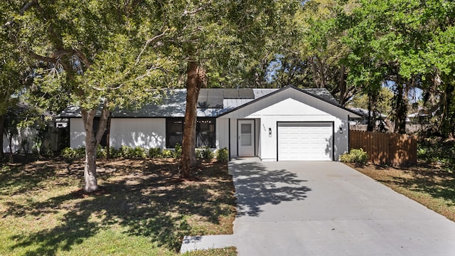 ranch-style home featuring a garage, concrete driveway, fence, and metal roof