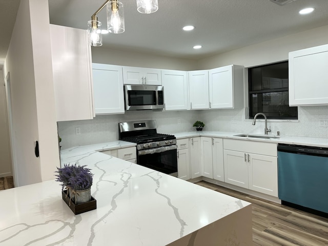 kitchen with decorative light fixtures, stainless steel appliances, white cabinetry, a sink, and light wood-type flooring