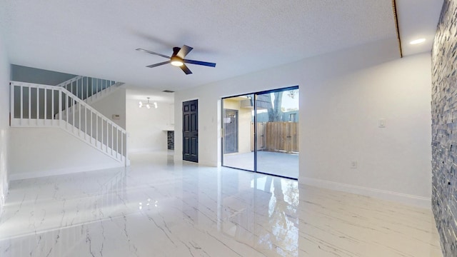 empty room featuring a textured ceiling, ceiling fan with notable chandelier, baseboards, marble finish floor, and stairway