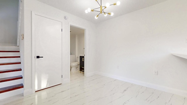 spare room with marble finish floor, a textured ceiling, baseboards, and a notable chandelier