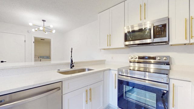 kitchen featuring a textured ceiling, stainless steel appliances, a sink, white cabinetry, and washer and clothes dryer