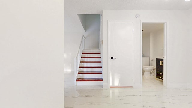 stairway with marble finish floor, baseboards, and a textured ceiling