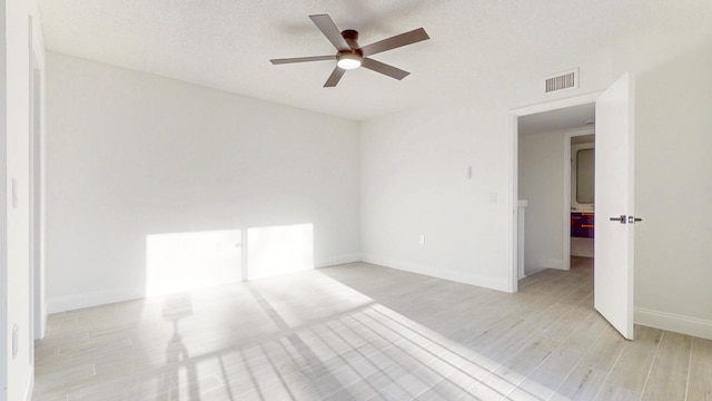 empty room featuring baseboards, visible vents, a ceiling fan, light wood-style flooring, and a textured ceiling