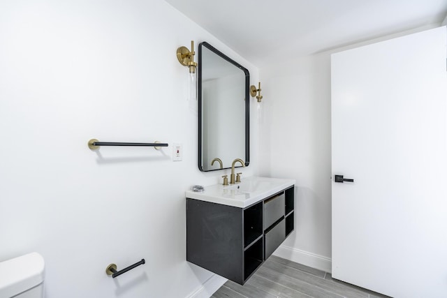 bathroom with toilet, baseboards, wood finished floors, and vanity