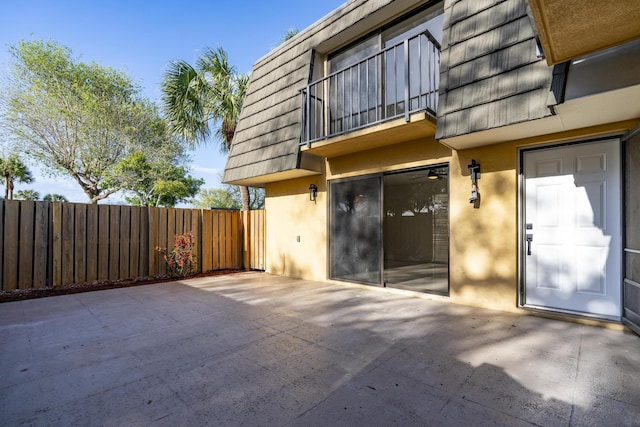 doorway to property with a patio area, fence, mansard roof, and stucco siding