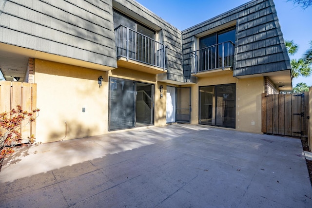 back of property with mansard roof, a patio area, fence, and stucco siding