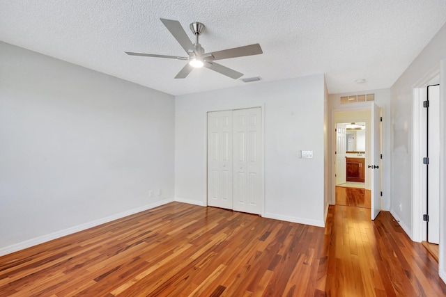 unfurnished bedroom featuring ceiling fan, a textured ceiling, a closet, and hardwood / wood-style floors