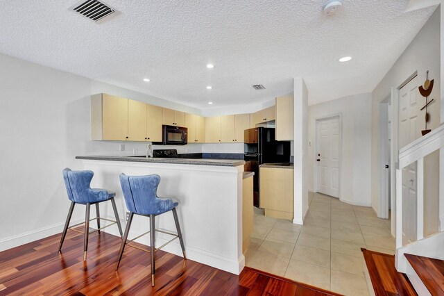 kitchen with light wood-type flooring, a textured ceiling, black appliances, kitchen peninsula, and cream cabinets