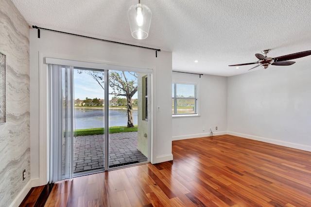 interior space featuring ceiling fan, a water view, a textured ceiling, and hardwood / wood-style floors