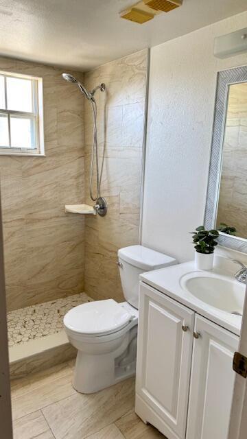 bathroom with a tile shower, vanity, and toilet