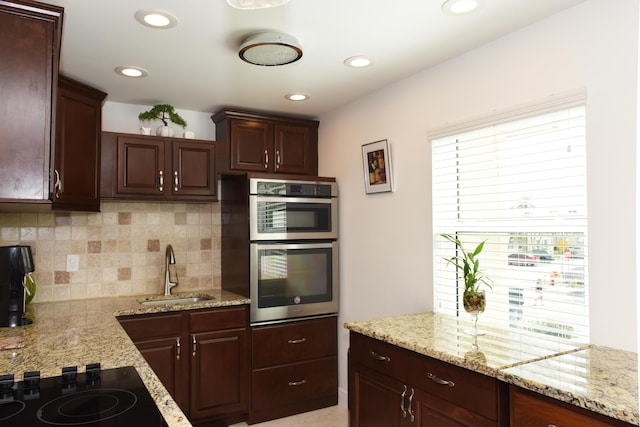 kitchen with sink, light stone counters, stainless steel double oven, black electric stovetop, and decorative backsplash