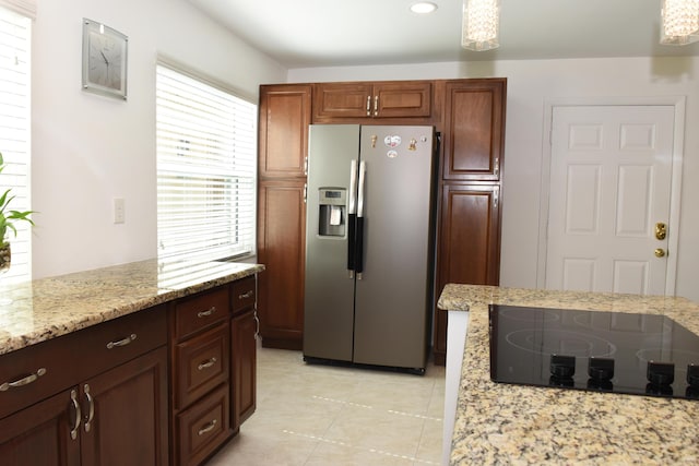 kitchen featuring light stone countertops, light tile patterned floors, stainless steel fridge, and black electric cooktop