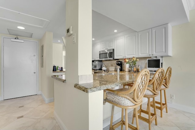 kitchen with a breakfast bar, tasteful backsplash, kitchen peninsula, light stone countertops, and white cabinets