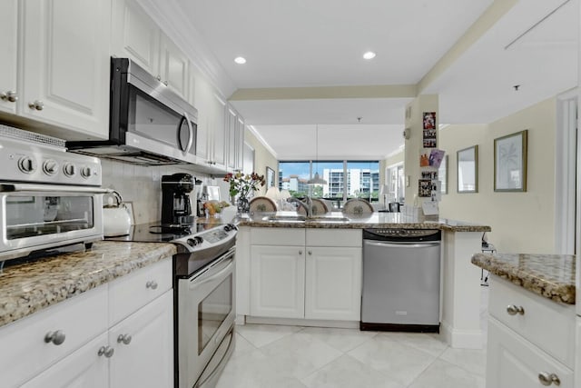 kitchen with white cabinetry, stainless steel appliances, light stone counters, decorative backsplash, and kitchen peninsula