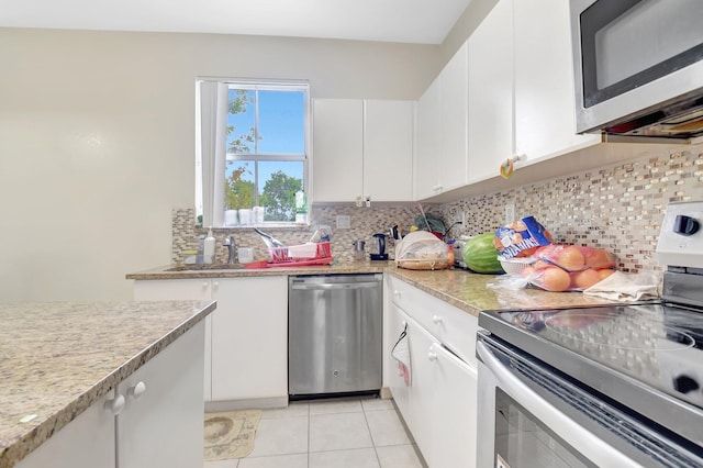 kitchen with light tile patterned floors, tasteful backsplash, white cabinets, appliances with stainless steel finishes, and light stone counters