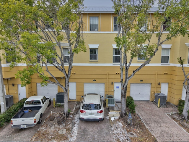 view of front of home with stucco siding, central air condition unit, an attached garage, metal roof, and driveway