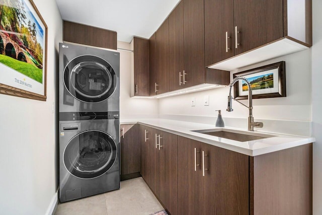 clothes washing area featuring light tile patterned flooring, cabinets, stacked washer and clothes dryer, and sink