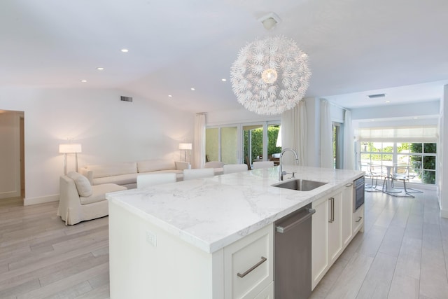 kitchen with an island with sink, open floor plan, stainless steel appliances, white cabinetry, and a sink