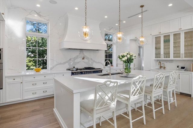 kitchen with sink, a breakfast bar area, custom range hood, and a center island with sink