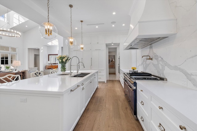 kitchen featuring stainless steel stove, white cabinets, hanging light fixtures, custom range hood, and a spacious island