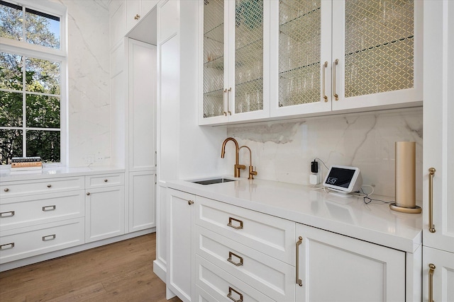 bar with white cabinetry, sink, decorative backsplash, and light wood-type flooring