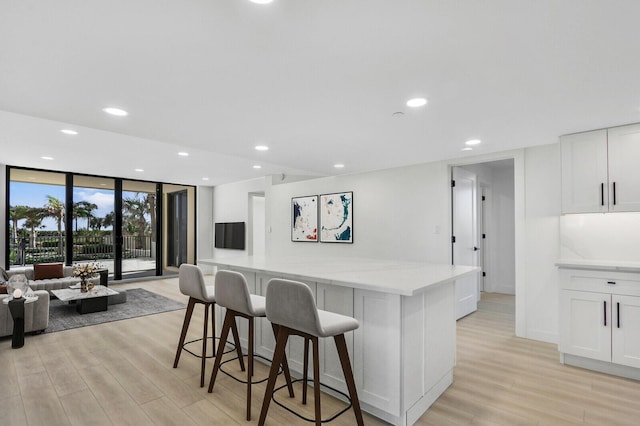 kitchen with expansive windows, white cabinetry, light stone countertops, and a breakfast bar area