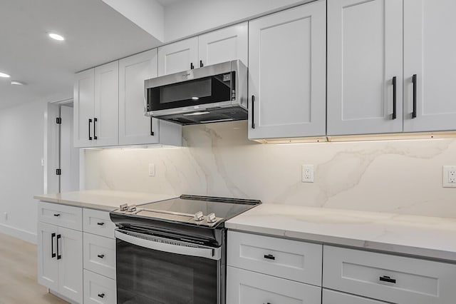 kitchen with appliances with stainless steel finishes, white cabinets, decorative backsplash, light stone counters, and light hardwood / wood-style flooring