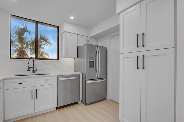 kitchen featuring sink, white cabinetry, light hardwood / wood-style flooring, stainless steel appliances, and backsplash