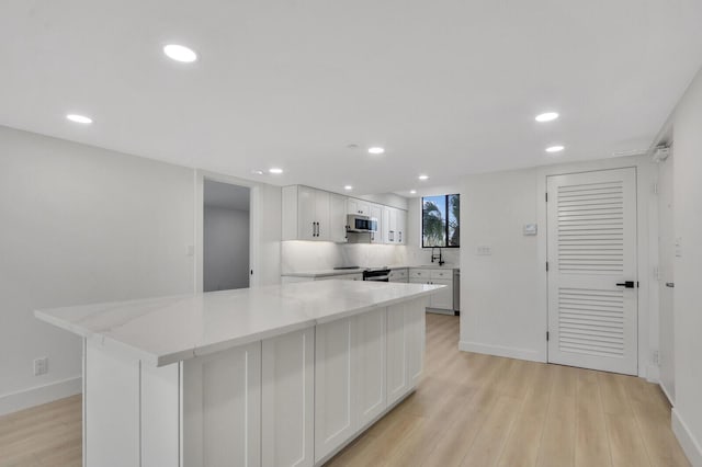 kitchen featuring a kitchen island, white cabinetry, sink, stainless steel appliances, and light stone countertops