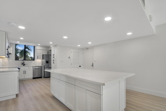 kitchen with sink, appliances with stainless steel finishes, a kitchen island, light stone countertops, and white cabinets