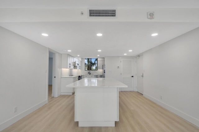 kitchen featuring white cabinetry, stainless steel appliances, a kitchen island, and light wood-type flooring