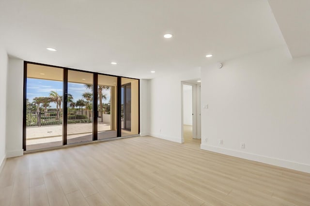 spare room with a wall of windows and light hardwood / wood-style floors