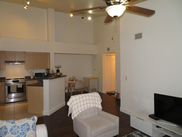 living area featuring baseboards, visible vents, a ceiling fan, a towering ceiling, and dark wood-style flooring