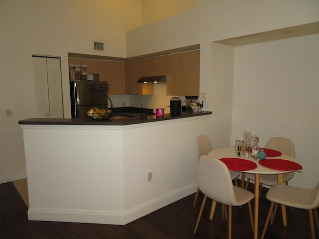 kitchen featuring under cabinet range hood, a peninsula, dark wood-type flooring, visible vents, and freestanding refrigerator