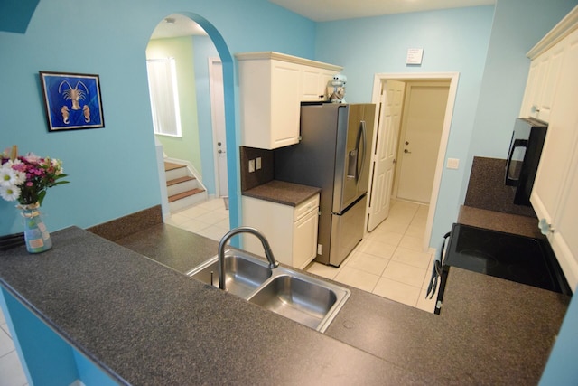 kitchen with arched walkways, a sink, black appliances, white cabinets, and dark countertops