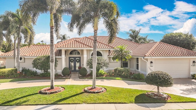 mediterranean / spanish home featuring french doors, stucco siding, concrete driveway, a garage, and a front lawn